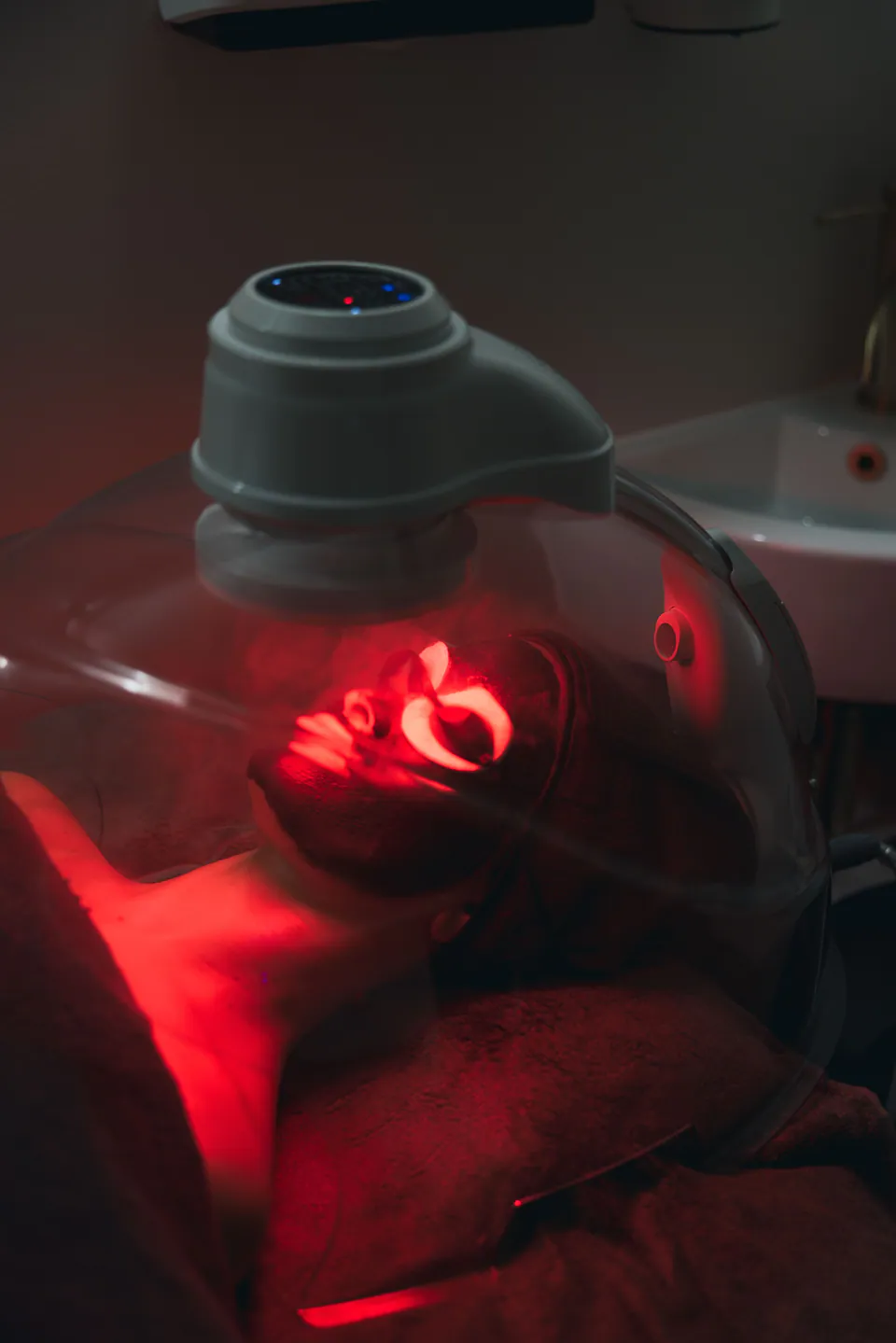 The Astrodome in use in a darkened treatment room, the client's face lit by red light beneath the dome