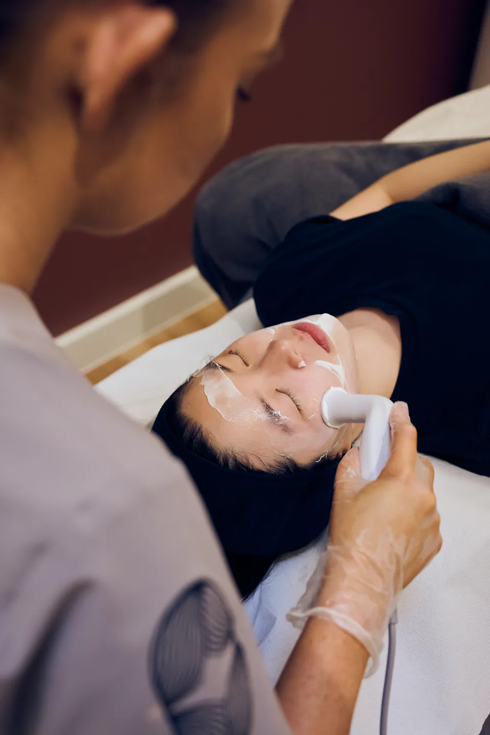 Close view of the Rexonage 3 handpiece being glided across a patient's face over conductive gel
