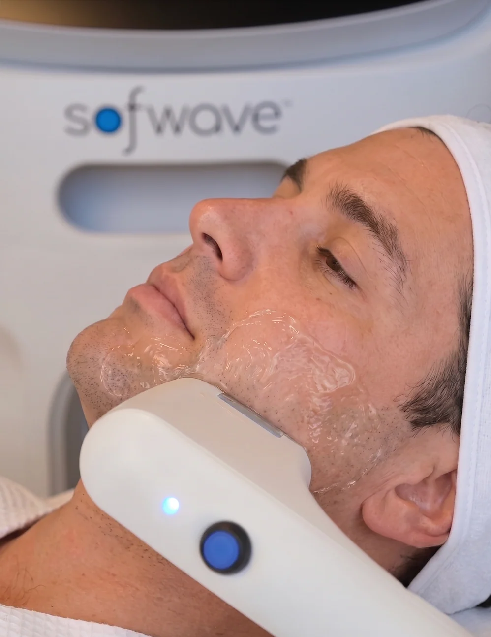 Close view of the Sofwave transducer being worked along a client's jawline over ultrasound gel