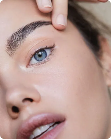Close view of a woman's face and eye, a fingertip resting at her brow