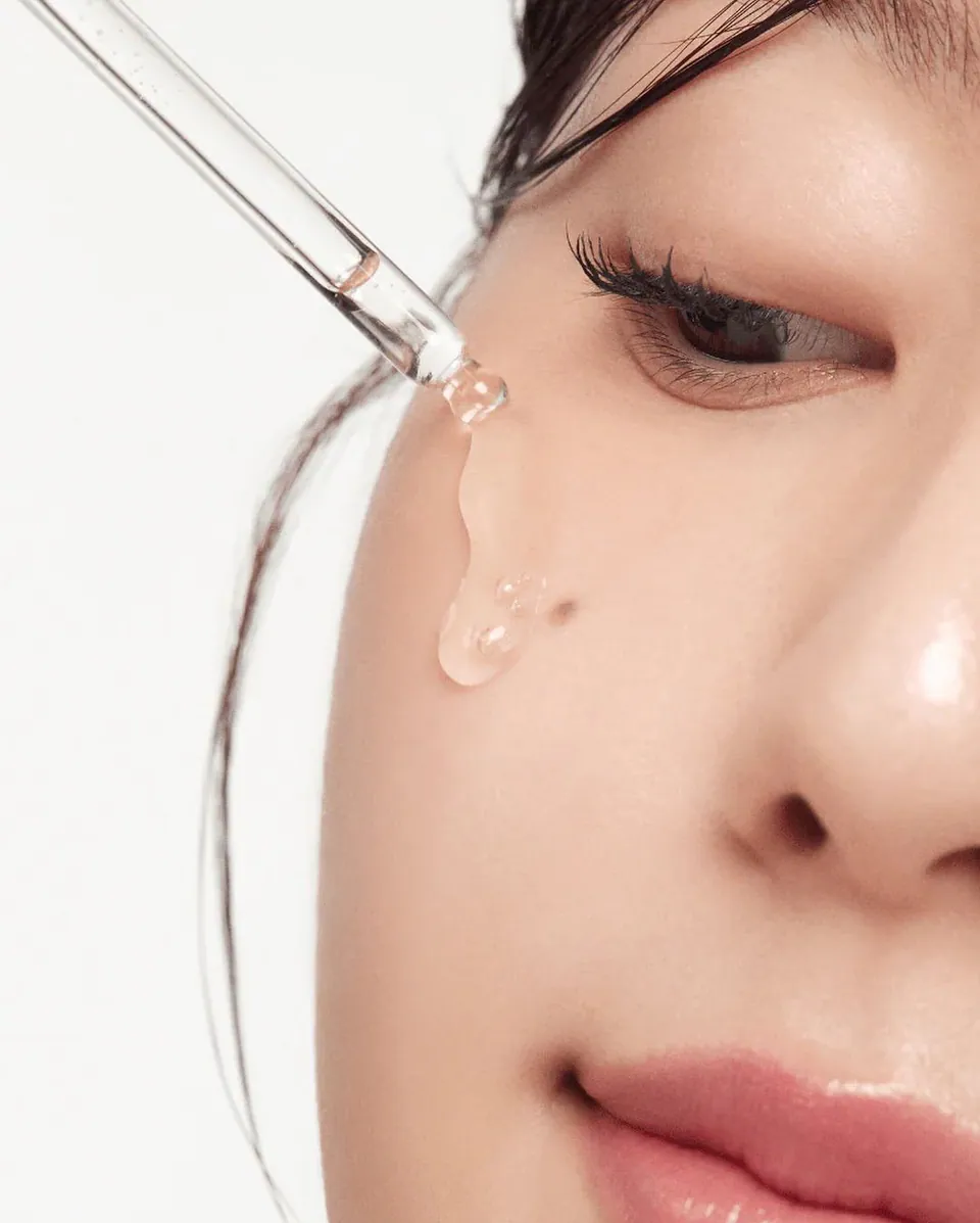 A dropper releasing clear serum onto a woman's cheek