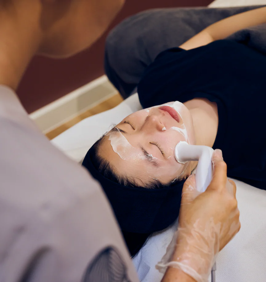 A facial treatment in progress, a handpiece being worked across a patient's face