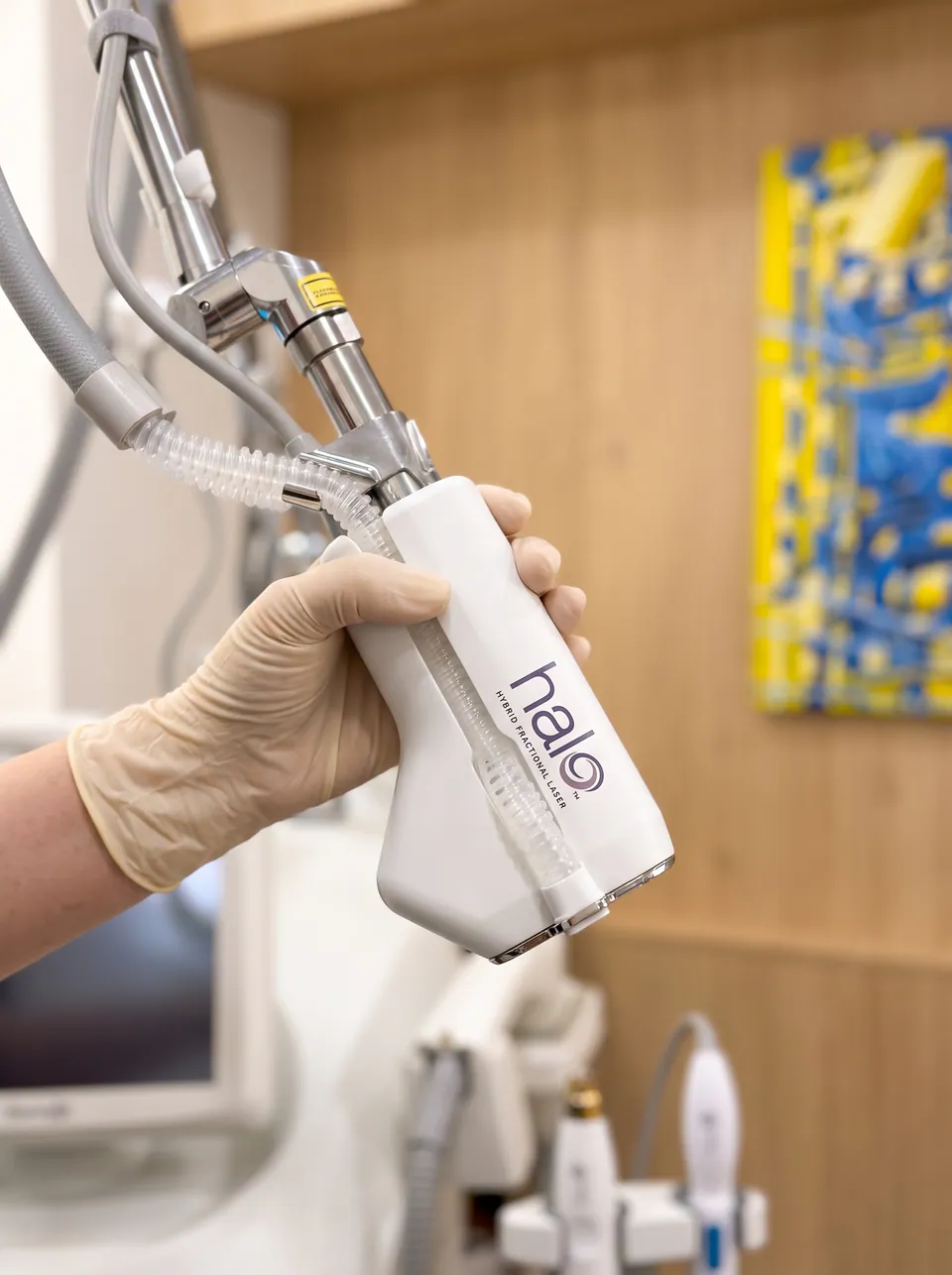 A gloved hand holding the Halo hybrid fractional laser handpiece on its articulated arm