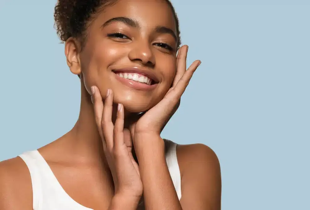 Smiling woman with clean skin holding her face after LED light therapy.