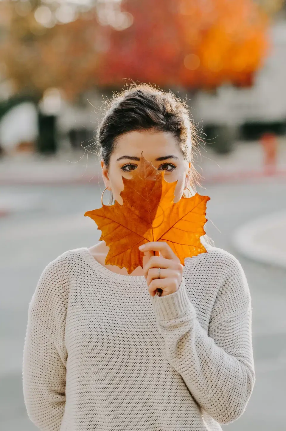 a woman with an autumn leaf in front of her face
