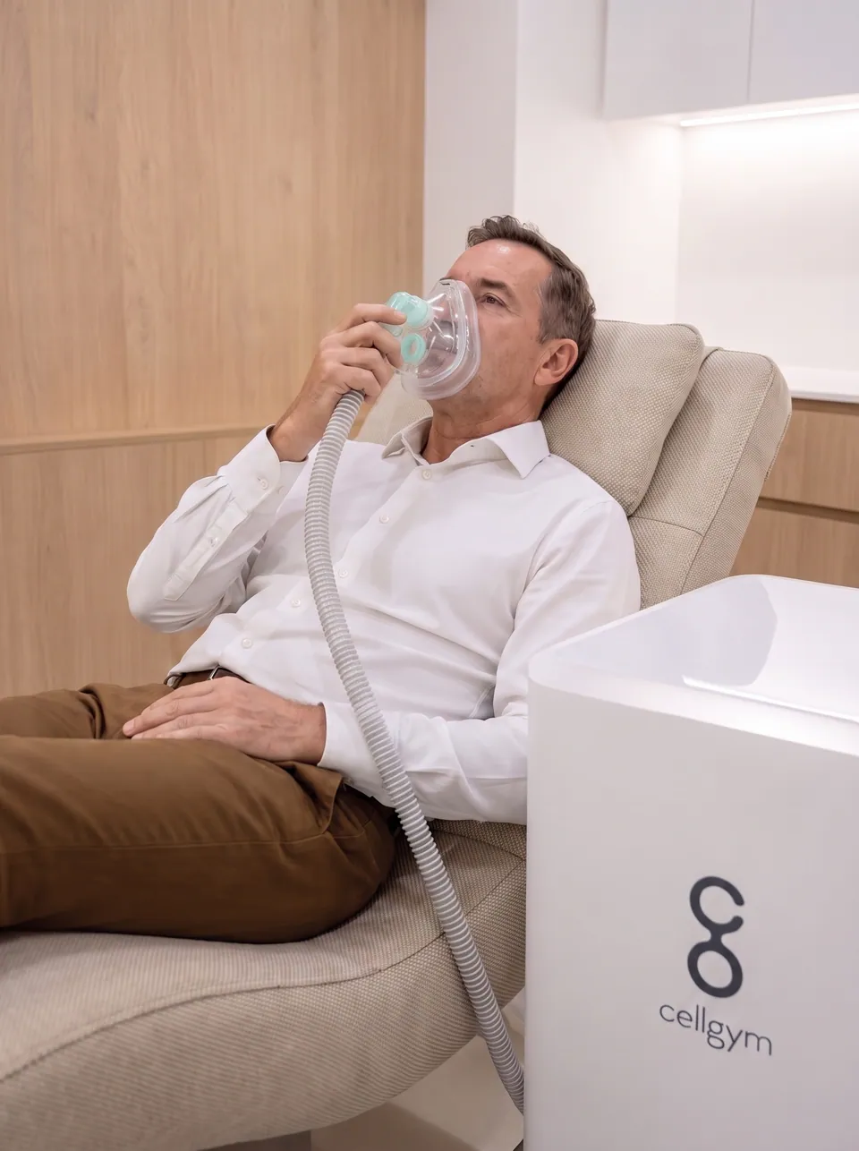 A man reclining in a treatment chair breathing through the CellAir mask, the cellgym unit beside him