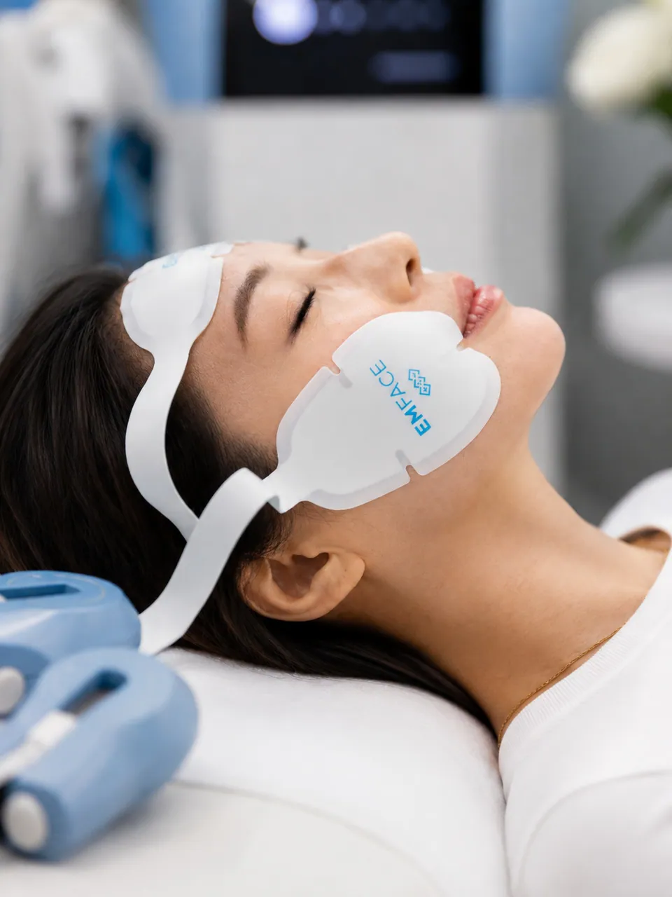 A patient lying back with EMFACE applicators on her forehead and cheek