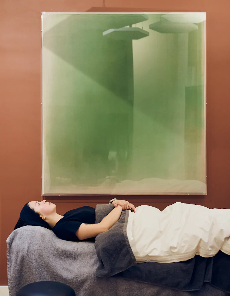 A patient resting on the treatment bed beneath a large green artwork on a terracotta wall