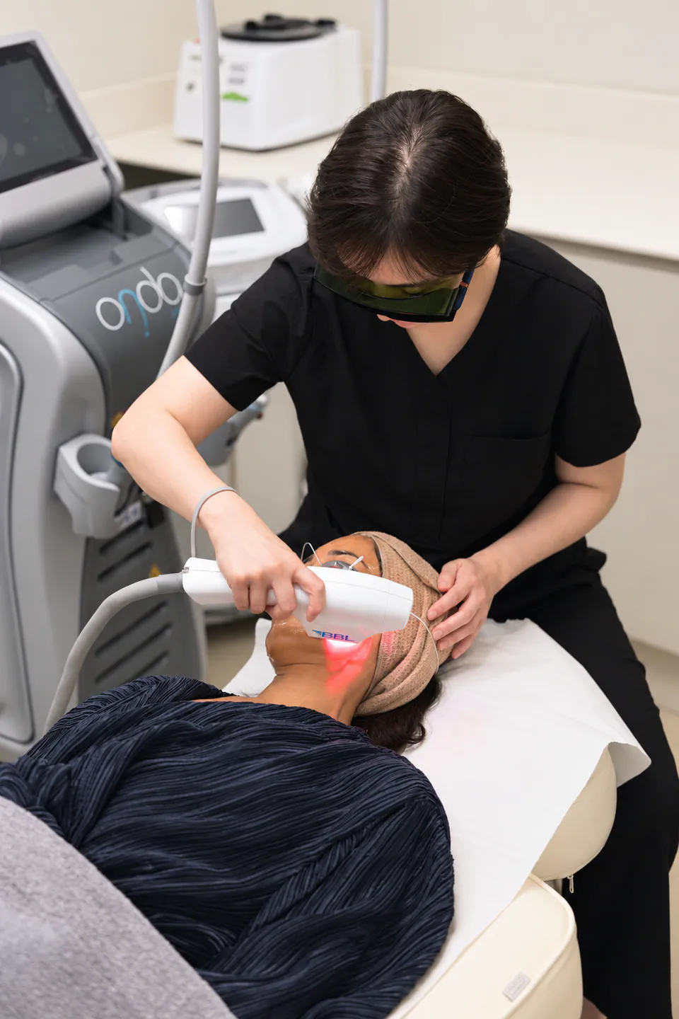 A practitioner delivering a BBL treatment along a client's jawline, eyes shielded and gel applied