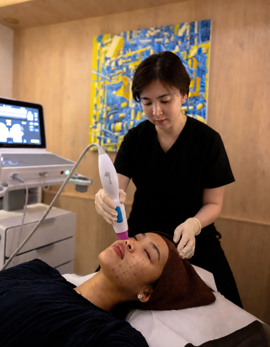 A practitioner delivering a Thermage treatment along a client's jawline, the treatment grid marked on the skin
