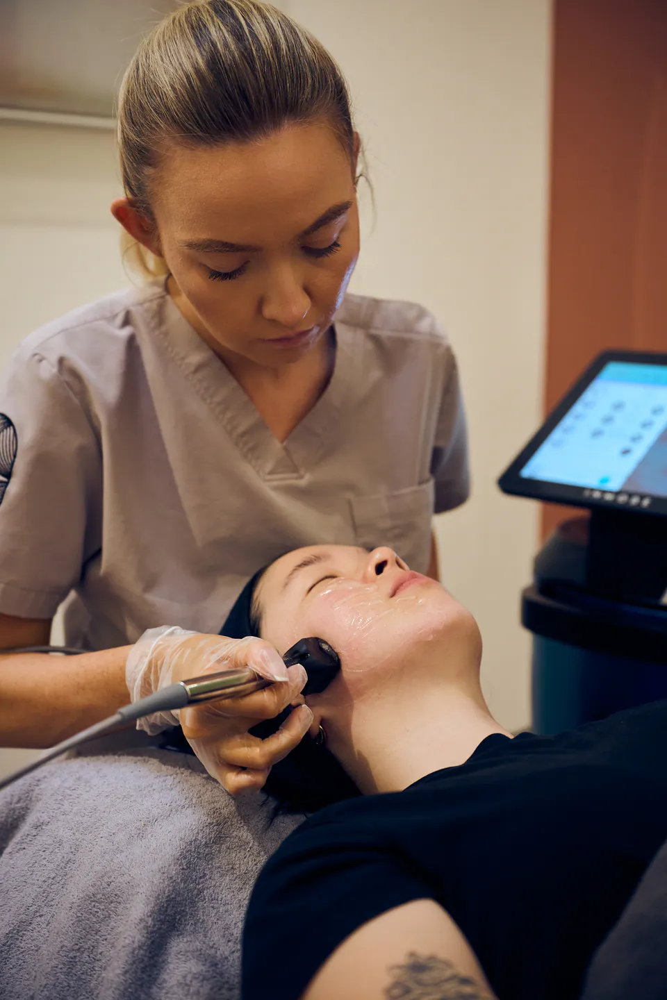 A practitioner guiding the InMode applicator along a client's jawline, the console screen beside her