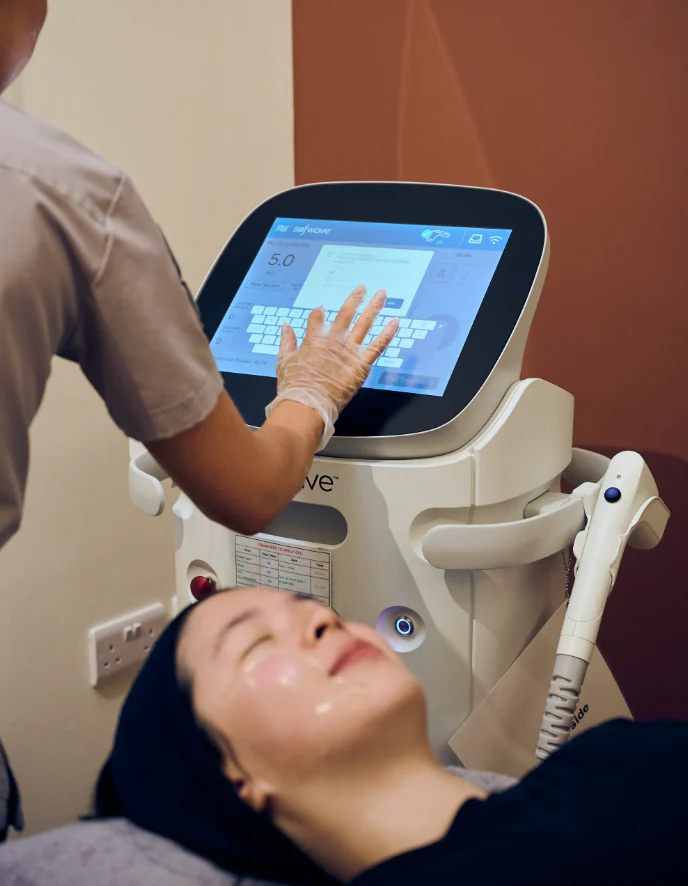 A practitioner setting the pulse duration on the Sofwave console while a client rests beneath it