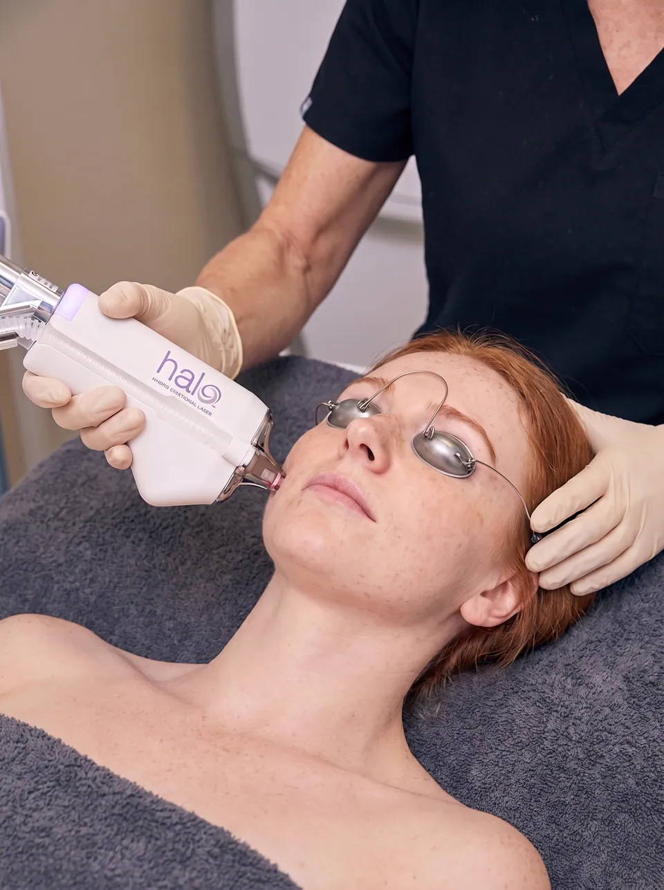 A practitioner treating a patient's cheek with the Halo handpiece, eyes protected by laser shields