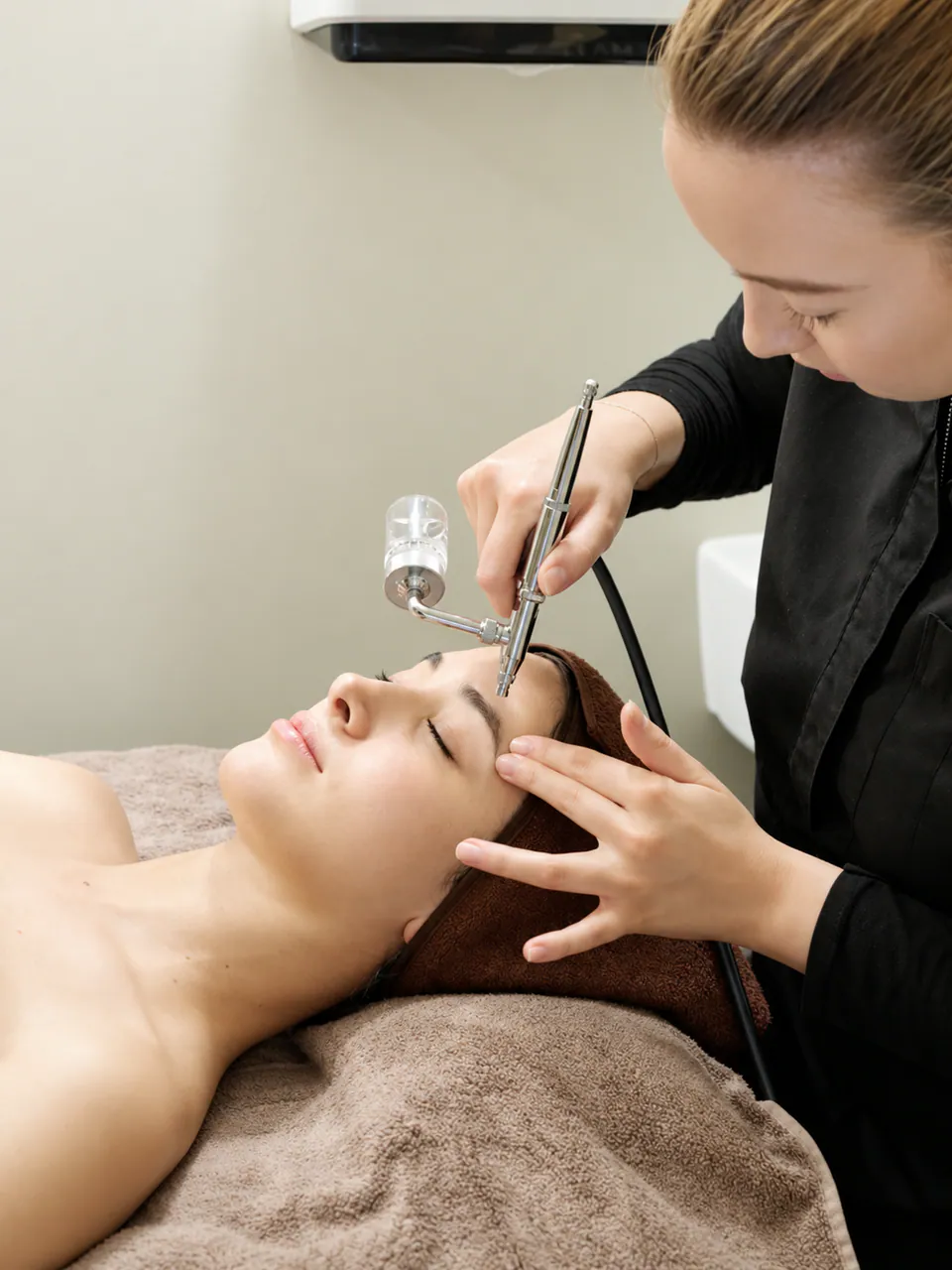 A therapist applying an oxygen serum mist across a client's face at the end of the treatment
