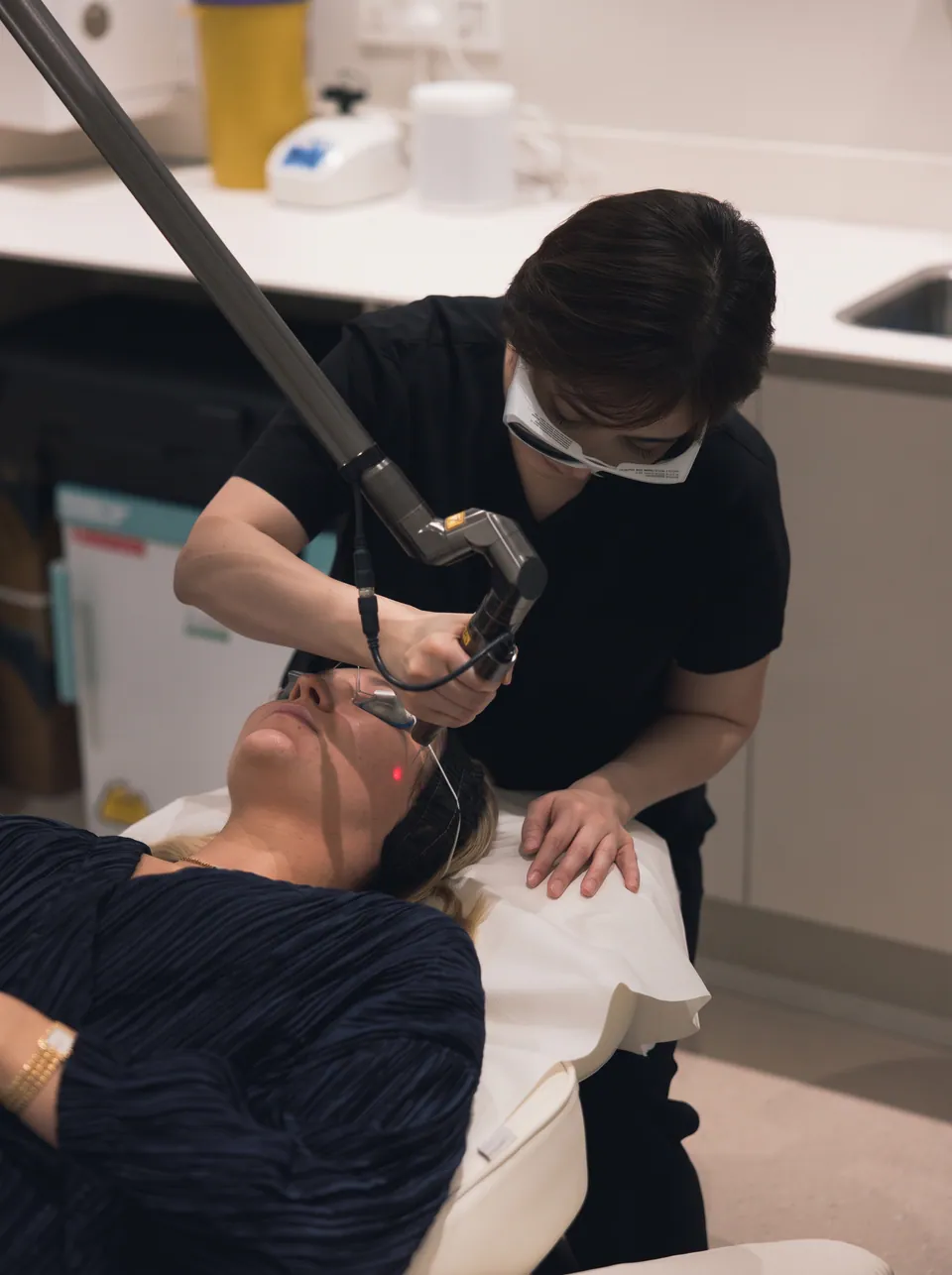 A therapist delivering a Hollywood Spectra treatment to a patient's face, the articulated arm guided across the skin