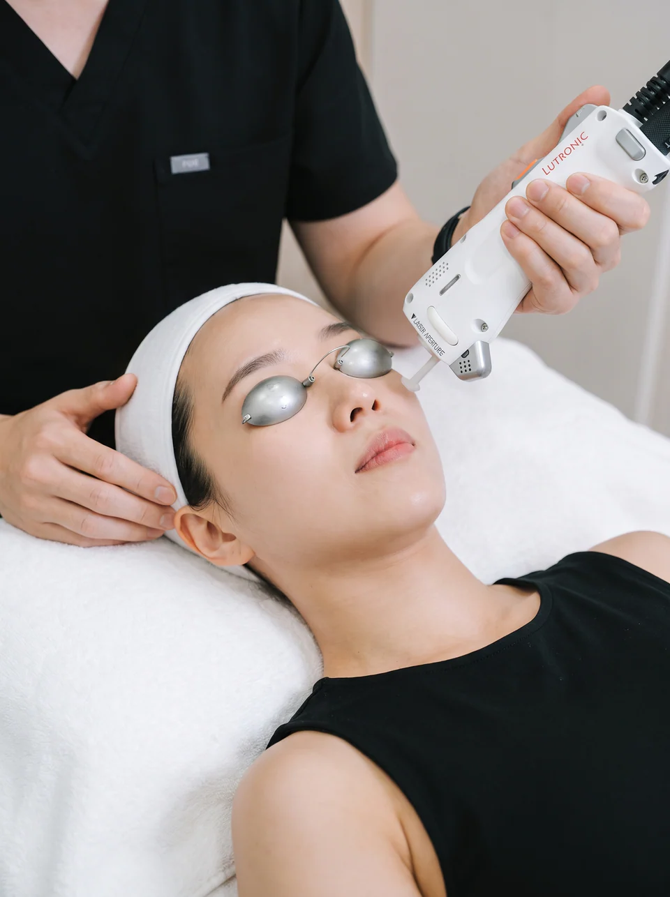A therapist guiding the Clarity II handpiece across a patient's cheek, her eyes protected by laser shields