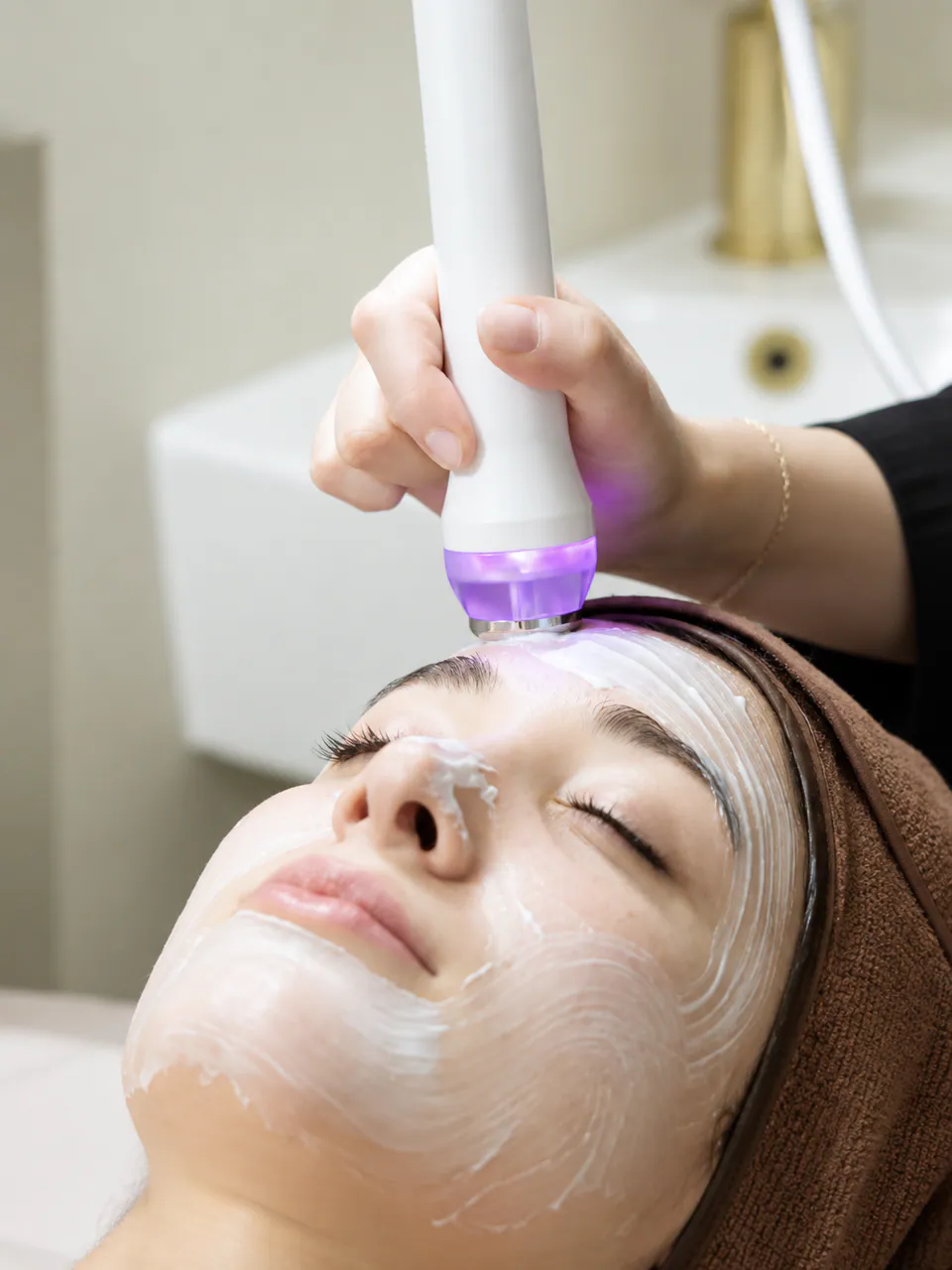 A therapist passing the HIFULDM handpiece across a client's forehead over a layer of treatment cream
