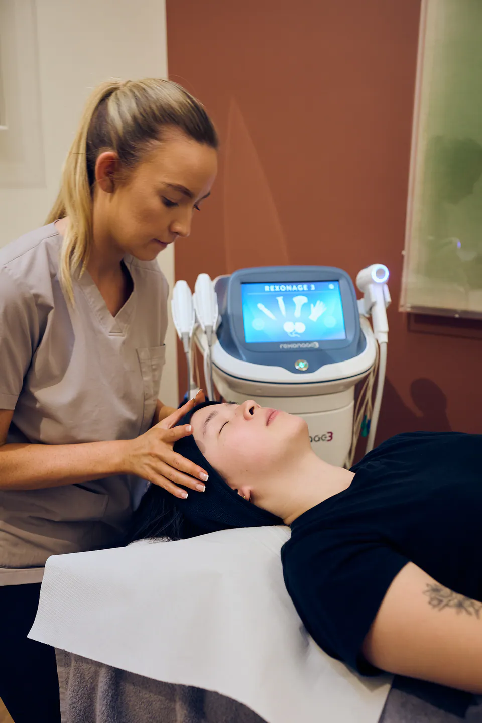 A therapist preparing a patient for a Rexonage 3 treatment, the device console beside the couch