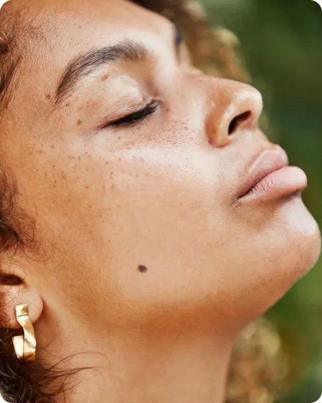 A woman with freckled skin in profile, eyes closed, in warm daylight