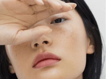 A woman with freckled skin shading her eyes with one hand