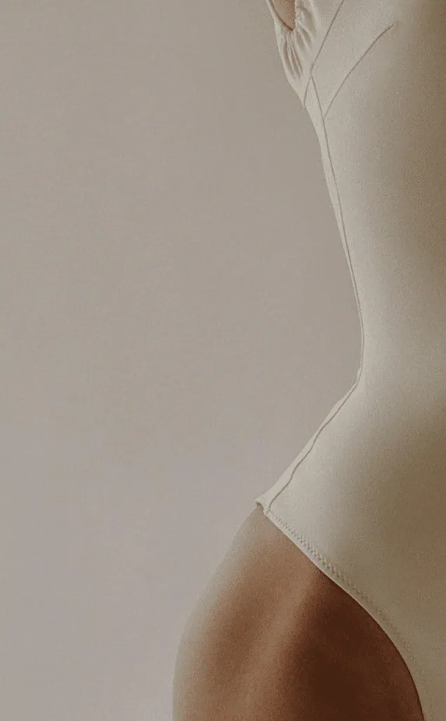 A woman in a pale bodysuit, photographed from the side