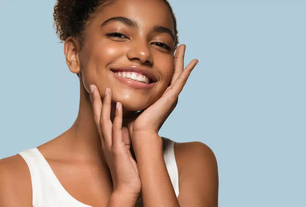 Smiling woman with clean skin holding her face after LED light therapy.