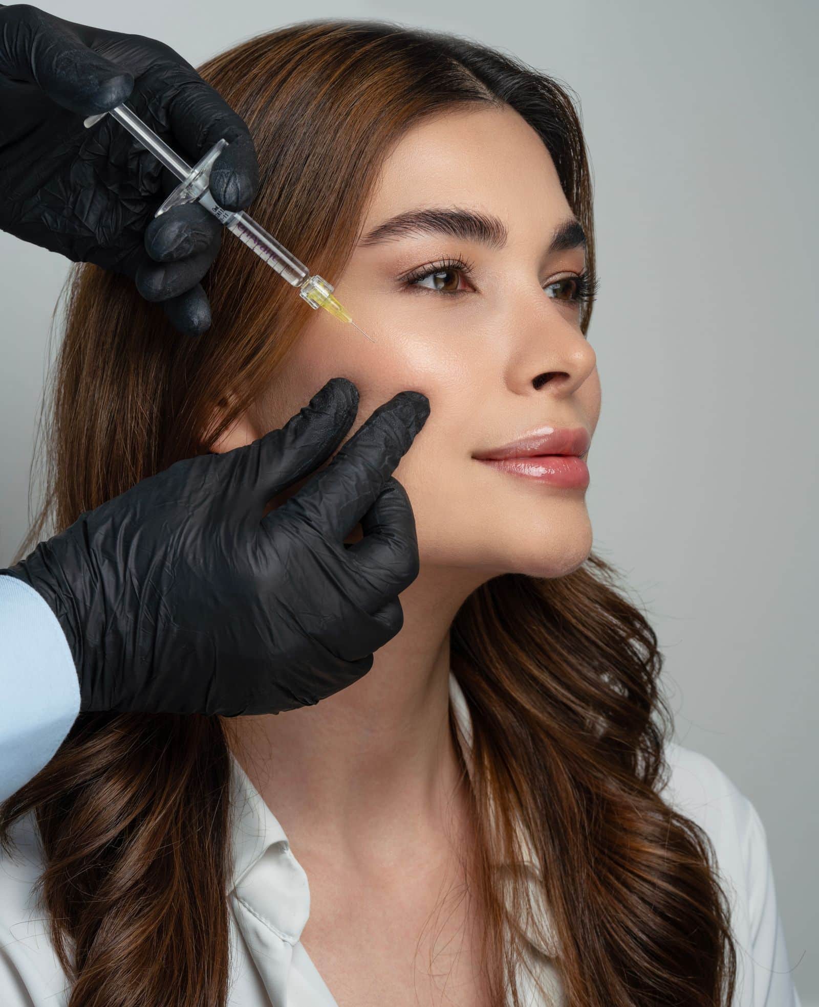 Consultant administering a dermal filler injection to a woman's cheek in clinic